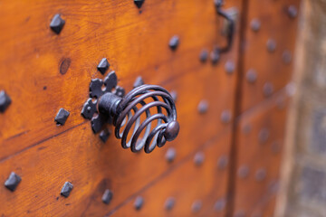 A close-up of an old wooden door displays an ornate metal handle and numerous studded details.