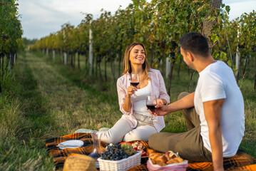 Couple enjoying a romantic picnic with wine in a vineyard during golden hour