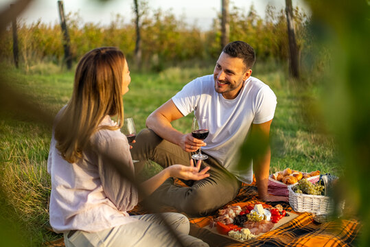 Couple enjoying a romantic picnic with wine and charcuterie in a vineyard - Powered by Adobe