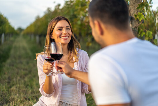 Couple toasting with red wine glasses in a vineyard during a romantic date - Powered by Adobe