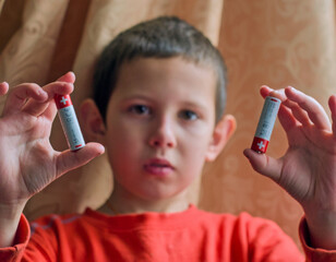 Child holding AA batteries - A child in a red shirt holds up two AA batteries, looking directly at the camera
