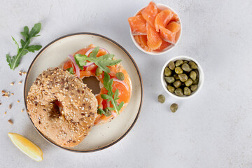 Bagel with salmon, cream cheese, cucumber and arugula on white background. Top view. 
