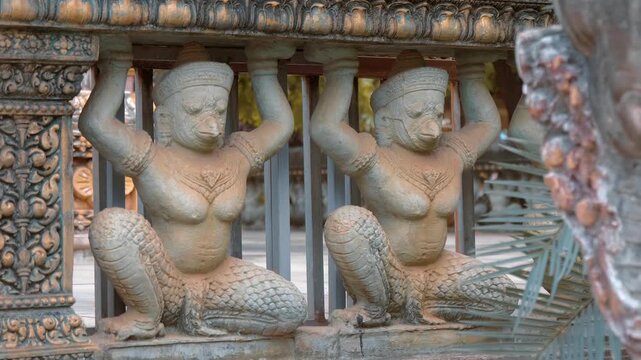 Stone statues of Garuda (mythical bird-like creatures) are supporting the roof in a Khmer temple garden in Siem Reap, Cambodia. Shot in motion