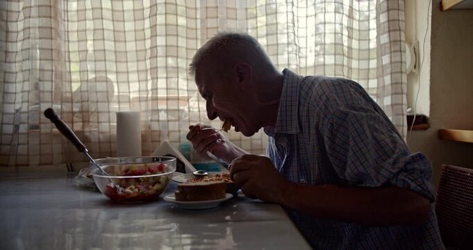 Observing an elderly man as he eats a healthy meal at his kitchen table. The scene, illuminated by natural light, captures a quiet, thoughtful moment and includes authentic sounds.