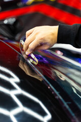Trimming purple chameleon tint on car windshield with precision knife, creating smooth, bubble-free edges. Windshield tint trimming purple chameleon film on car windshield in detailing.