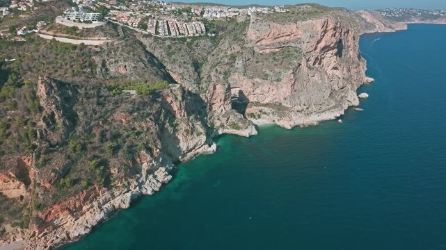 Aerial drone footage of Cala del Moraig cliffs and Mediterranean coast with houses and turquoise water in Benitatxell, Spain. Beautiful view of the Costa Blanca coastline.