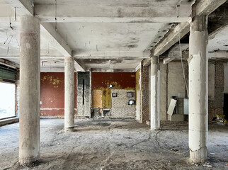 Abandoned industrial interior with exposed concrete columns, damaged walls, and remnants of old paint, showing signs of decay and partial demolition.