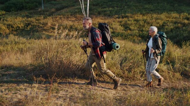 Mature couple with backpacks goes uphill together at countryside