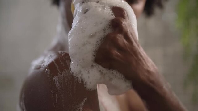 Young adult African American woman washing herself with sponge and gel shower, enjoying bath procedures relaxing at home. Selective focus of black millennial female doing your daily skin care routine 