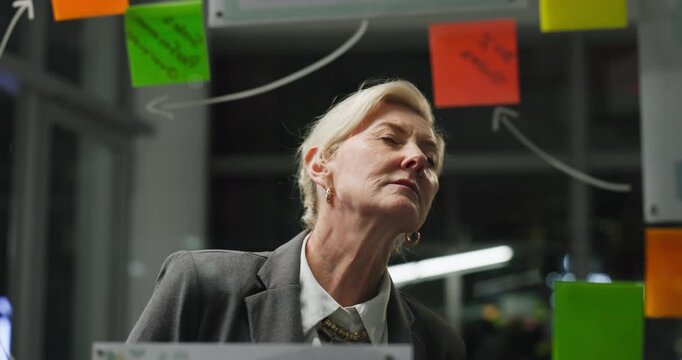 Glass wall, reading or woman in office at night, campaign or creative strategy in brainstorming. Sticky note, bokeh or marketing director in agency with mind map, planning or ideas on late shift.