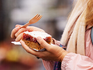 Close-up of a woman holding a fruit dessert and eating with a wooden eco fork at a farmers market in Prague.