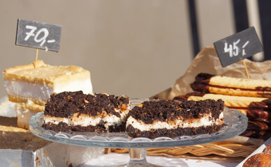 Display of homemade desserts at a farmers market stall in Prague, featuring cakes and pastries on a glass stand.