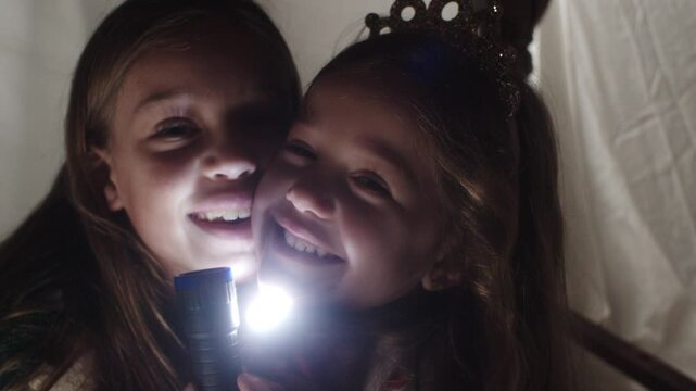 Girls having fun playing flashlight games under a sheet in the living room