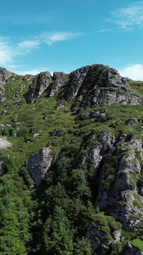 Rocky peaks of Babin Zub mountain in Stara Planina National Park, Serbia, rise above green forests under a blue sky. Aerial view from drone. Vertical 4k footage