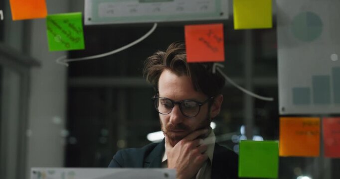 Glass wall, reading or person in office at night, campaign or creative strategy in brainstorming. Sticky note, bokeh or marketing director in agency with mind map, planning or ideas on late shift.