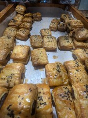 Freshly baked golden puff pastries with a savory filling, topped with black sesame seeds on a tray.