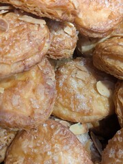 Close-up of golden, flaky pastries, possibly almond croissants, with sugar and nuts.