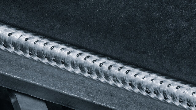 Close-up of metal part with weld seam, the part lies on metal production table in factory or telloconstruction plant as industrial metal concept background