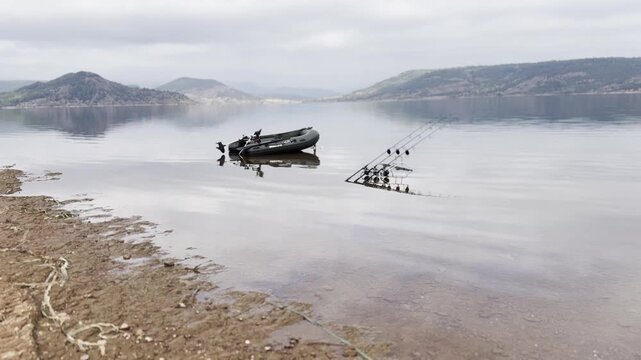 Three carp fishing rods set up with inflatable dinghy on the shore of Salagou Lake in southern France. Typical scene of carp angling. Check my portfolio for more Salagou footage.