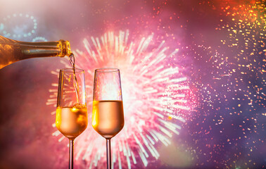 two glasses of champagne clink against the backdrop of New Year's fireworks