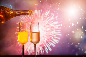 two glasses of champagne clink against the backdrop of New Year's fireworks