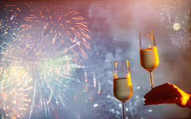 two glasses of champagne clink against the backdrop of New Year's fireworks