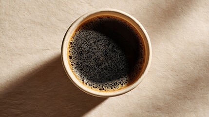 Top view captures dark, hot beverage with foam resting on textured, light surface