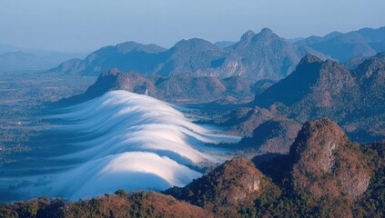 Rolling clouds cascade through a mountain valley in morning light.