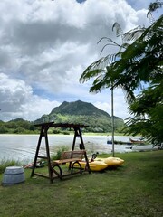 Lakeside tranquility A wooden swing and bright kayaks on green grass, with a majestic mountain and cloudy sky, perfect for peaceful outdoor escape