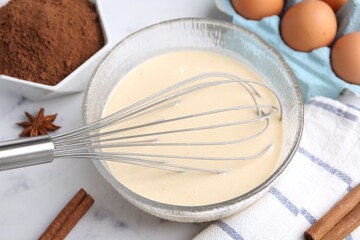 Liquid dough in bowl, whisk and ingredients on white table, closeup