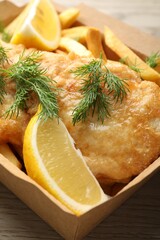 British Traditional Fish and chips with lemon in paper box on wooden table, closeup