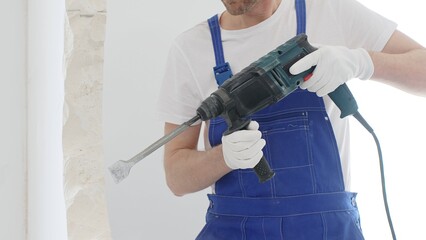Unrecognizable male construction worker wearing blue overalls and protective white gloves, is...