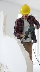 Male construction worker wearing red checkered shirt, yellow hard hat and protective gloves, is...