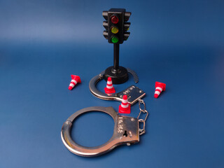 The image is a conceptual stock photo that combines a traffic light, handcuffs, and traffic cones...