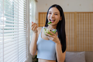Sporty Girl Enjoying Vegetable Salad Standing Holding Bowl Over Near Window In Studio. Healthy Nutrition And Fitness