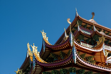 Fototapeta premium The Elegant Upturned Eaves and Ornate Details of Traditional Chinese Architecture Against a Clear Blue Sky