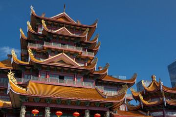 A Multi-Story Temple Featuring Traditional Chinese Architectural Style with Ornate Roofs and Red Lanterns Against a Clear Blue Sky