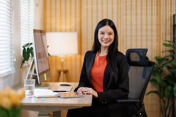 Young asian business woman managing documents and computer screens at corporate office desk,...