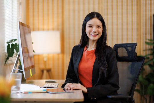 Young asian business woman managing documents and computer screens at corporate office desk, smiling while working.
- Powered by Adobe