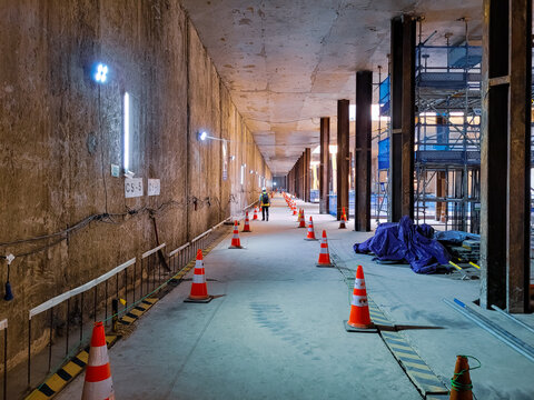 Underground construction hallway with steel support columns, safety cones, lighting, and scaffolding, showing active civil engineering and structural development work.