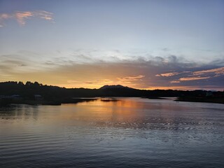 Fototapeta premium Serene sunset over calm river reflecting golden sky and distant hills