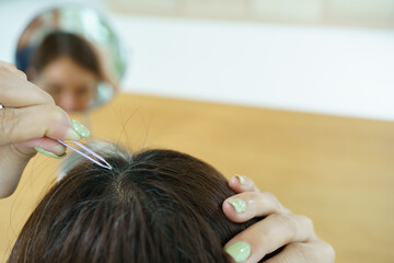 Naklejka premium Top view of Asian woman removing gray hair with tweezers at home.