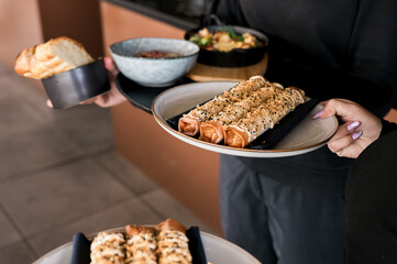 Close-up of a waiter holding plates with gourmet appetizers,fresh bread,and sauce bowls in a stylish modern restaurant.Concept of fine dining,professional service,and contemporary cuisine presentation