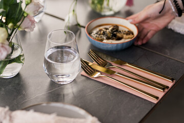 A refined dining setup with gold cutlery, fresh flowers, and a bowl of food being served, capturing an elegant and intimate meal moment.