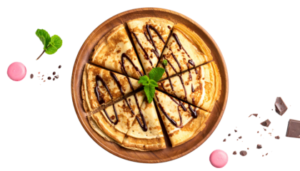 Overhead view of sliced crepes drizzled with chocolate, mint sprig, macarons, and chocolate bits