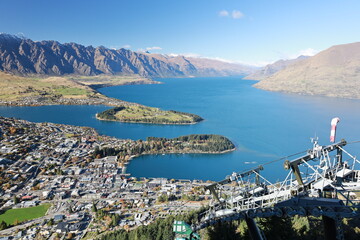 An aerial view of Queenstown, New Zealand, from the Skyline Gondola in May 2025. The vibrant town, Lake Wakatipu's blue waters, and distant mountains create a stunning panorama.
