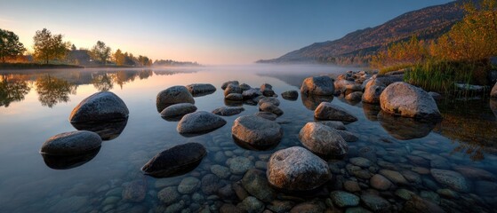 Tranquil lake scene with stones and reflections at sunrise or sunset