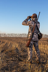 hunter with shotgun looking through binoculars in field.