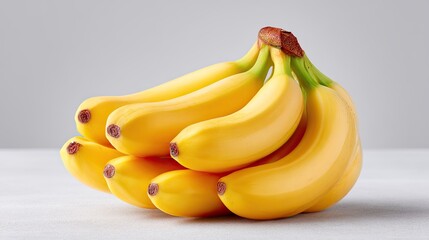 A Bunch Of Ripe Yellow Bananas With Green Stems Sitting On A White Surface With A Light Gray Background