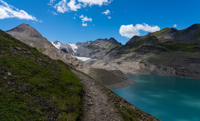 Turquoise Gries Lake and glacier near Corno-Gries Pass in the Swiss Alps. Stunning alpine landscape with rugged peaks, hiking trails, and wildflowers under a bright summer sky.